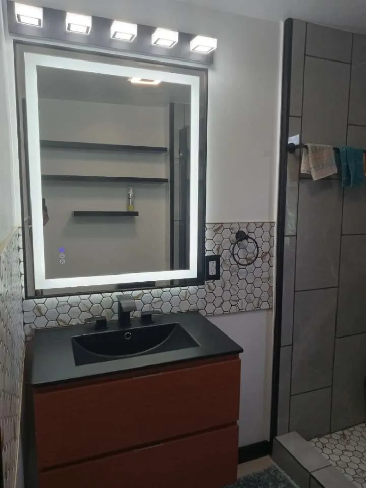 Bathroom vanity with a lit mirror and a tiled shower wall